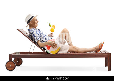 Full length profile shot of an elderly man lying on a sunbed drinking a cocktail and holding an inflatable beach ball isolated on white background Stock Photo