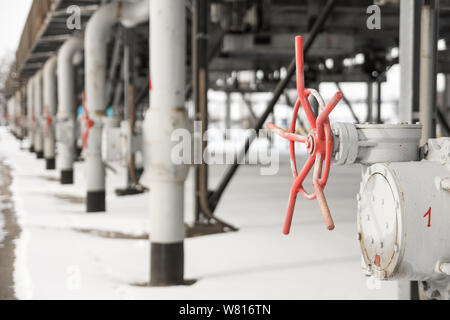 The grey metal tubes for gas delivering with red valves at gas compressor station shooted in winter. The view on a tube construction for gas transport Stock Photo