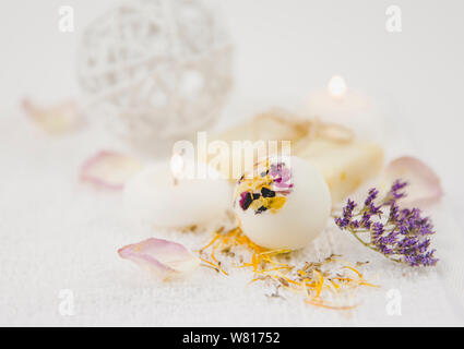 Beautiful set with selective focus on white creamy moisturizing small bath ball bomb with dry flower blossom petals, spa candles burning and dry flowe Stock Photo