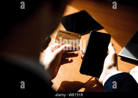 Upper view of male hand operating on a smartphone and using a gold credit card while sitting in office. Stock Photo