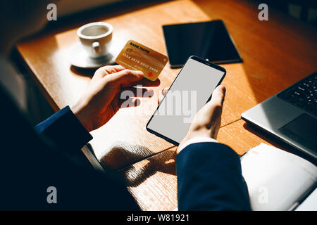 Close up of male hands holding a gold credit card and a smartphone doing online banking while drinking coffee in a coffee shop. Stock Photo