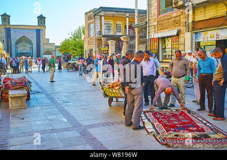 SHIRAZ, IRAN - OCTOBER 14, 2017: The carpet vendors and their providers check the carpets in the street of Vakil Bazaar with the portal of Vakil Mosqu Stock Photo