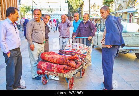 SHIRAZ, IRAN - OCTOBER 14, 2017: The group of carpet providers, merchants and porters with trolley cart, loaded with rugs, Vakil Bazaar, on October 14 Stock Photo