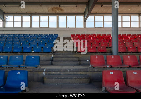 Front view row of blue and red plastic seats on rough concrete different level floor between stair in old vintage dirty concrete structural stadium. Stock Photo