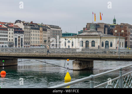 Man walk and run on pedestrian bridge cross Lake Geneva and Rhône rive, and background of Cité du Temps de Genève, Geneva's downtown and cloudy sky. Stock Photo