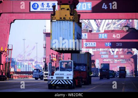 A crane vehicle lifts containers to be shipped abroad from trucks on a quay at the Port of Qingdao in Qingdao city, east China's Shandong province, 10 Stock Photo