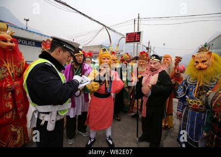 A police officer is surrounded by actors who were on their way to a 'Journey to the West' performance as he checks and registers the driving license o Stock Photo