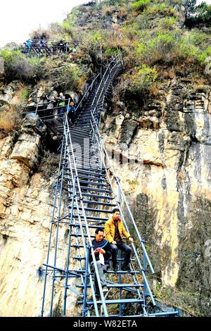 Tourists rest as they climb up an 800-meter cliff on a steel ladder in a mountainous area in Atuler village, Zhaojue county, Liangshan Yi autonomous p Stock Photo