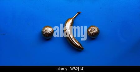 Abstract shot of golden plated bananas and mandarins on a blue background Stock Photo