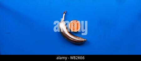 Abstract shot of golden plated bananas and mandarins on a blue background Stock Photo