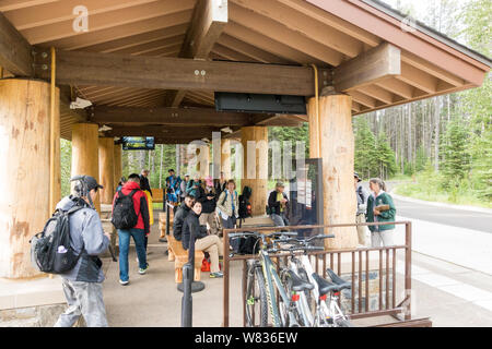 People waiting for shuttle at the bus stop at Apgar Visitor Center in Glacier National Park, Montana, USA Stock Photo