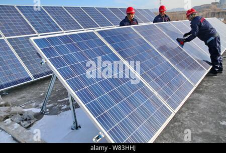--FILE--Chinese workers install solar panels on the rooftop of a building at a photovoltaic power station in Qinhuangdao city, north China's Hebei pro Stock Photo