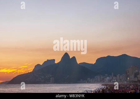 Amazing sunset at Rio de Janeiro litoral seen from Arpoador rock depicting Ipanema beach with a crowd on the sand and the silhouette of the mountains Stock Photo