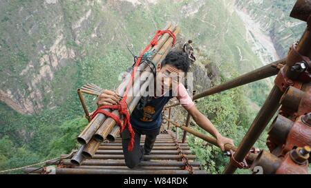 A Chinese villager carrying steel pipes climbs up a steel ladder on the ...