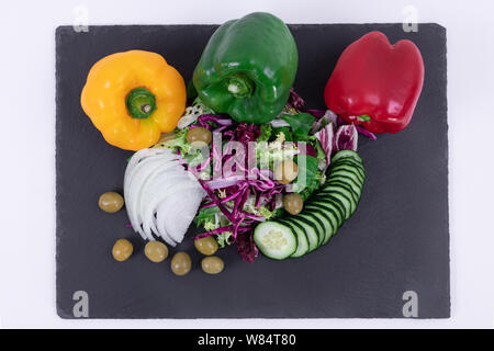 Top view of fresh vegetable salad - Olives, chopped onions, sliced cucumbers, purple cabbage on a black cutting board Stock Photo