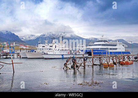View of ships in the port of Ushuaia against a landscape showing the city and the Martial mountains covered in snow, surrounded by a blue sky with whi Stock Photo