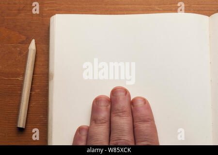 Man holding hand on old book with blank page on wooden table with a small pencil Stock Photo