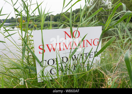 'No swimming, cold water can kill' sign by shore of Virginia Water Lake in summer, Windsor Great Park, Runnymede, Surrey, England, United Kingdom Stock Photo