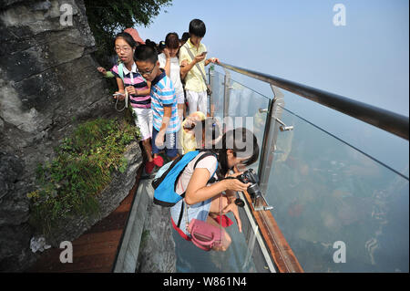 Tourists walk on the 100-meter-long and 1.6-meter-wide glass skywalk on the cliff of Tianmen Mountain (or Tianmenshan Mountain) in Zhangjiajie Nationa Stock Photo