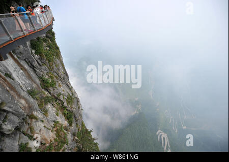 Tourists walk on the 100-meter-long and 1.6-meter-wide glass skywalk overlooking the 'Tianmen Tongtian Avenue' on the cliff of Tianmen Mountain (or Ti Stock Photo