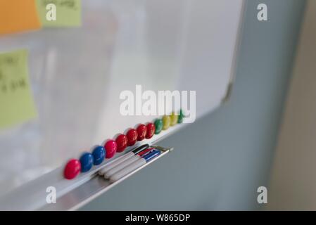 Closeup shot of a whiteboard with colorful pins and three markers on its tray shelf Stock Photo
