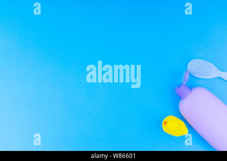 Blurry Flat lay composition of baby care products on a blue background. View from above shampoo or shower bottle gel, cleaning brush and yellow rubber Stock Photo