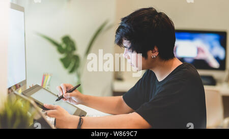 Young professional male photographer retouching his photos with digital tablet in comfortable workplace Stock Photo