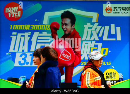 --FILE--Pedestrians walk past an advertisement for Suning.com, the online shopping site of home appliance chain Suning, in Yichang city, central China Stock Photo