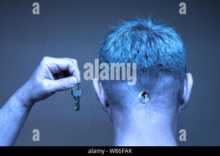 A man with a keyhole in the back of his head holds keys in a raised hand Stock Photo