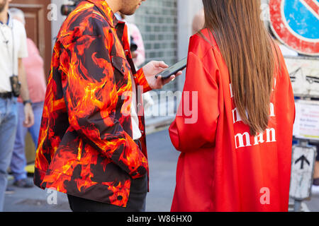 MILAN, ITALY - JUNE 16, 2019: Man with shirt with orange flames and woman with red dress before Etro fashion show, Milan Fashion Week street style Stock Photo