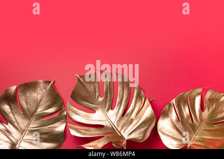 Exotic summer trend in minimal style. Golden tropical palm monstera leaf on red color background. Shiny and sparkle design, fashion concept Stock Photo