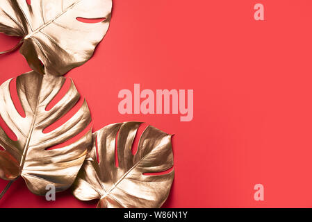 Exotic summer trend in minimal style. Golden tropical palm monstera leaf on red color background. Shiny and sparkle design, fashion concept Stock Photo