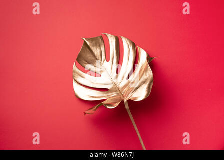 Exotic summer trend in minimal style. Golden tropical palm monstera leaf on red color background. Shiny and sparkle design, fashion concept Stock Photo