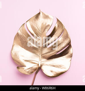 Floral minimal style concept. Exotic summer trend. Golden tropical palm monstera leaf on pastel pink color background. Shiny and sparkle design, fashi Stock Photo