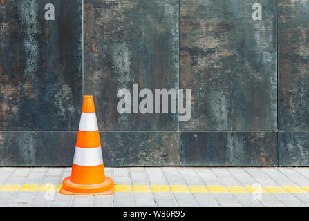 Plastic traffic cone against grunge wall with copy space, road cone and bollard standing on pavement Stock Photo