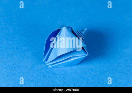 Blue origami seashell on blue background. Japanese art of paper folding. Flat square sheet of paper transferred into finished sculpture. Stock Photo