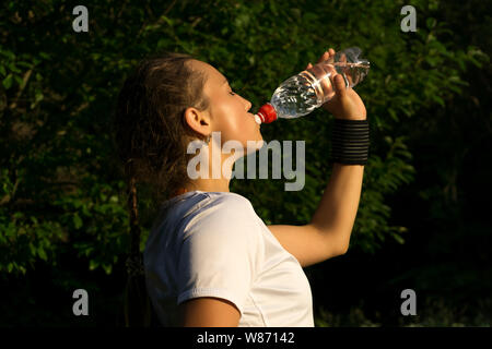 girl after playing sports in the park quenching thirst drinks water from the bottle Stock Photo