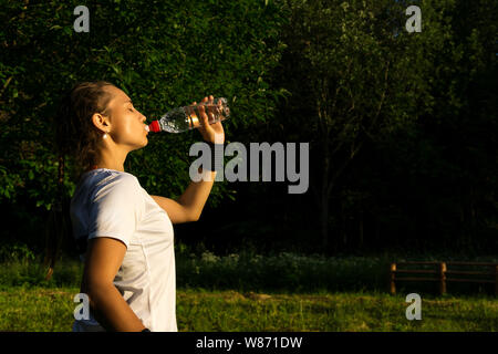 girl after playing sports in the park quenching thirst drinks water from the bottle Stock Photo