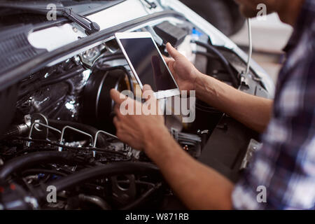 Close up of a man using his tablet to know how to fix car engine. Stock Photo