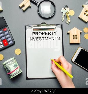 Table with wooden houses, calculator, coins, magnifying glass with the word Property investments. Attracting investment in your home. Repair planning. Stock Photo