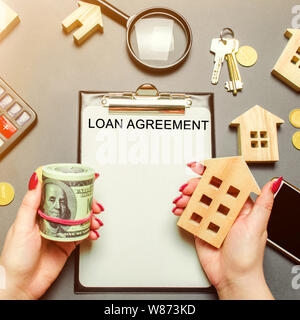 Table with wooden houses, calculator, coins, magnifying glass with the word Loan agreement. The contract for the purchase of a house or apartment on c Stock Photo