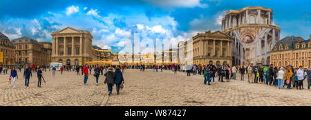 Large panorama picture of the famous Palace of Versailles near the golden royal gate where visitors are queuing at the entrance in the cobblestoned... Stock Photo