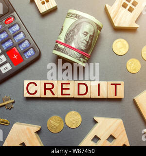 Table with wooden houses, calculator, coins, magnifying glass with the word Credit on wooden blocks. Buying a home in debt. Credit for a house or apar Stock Photo