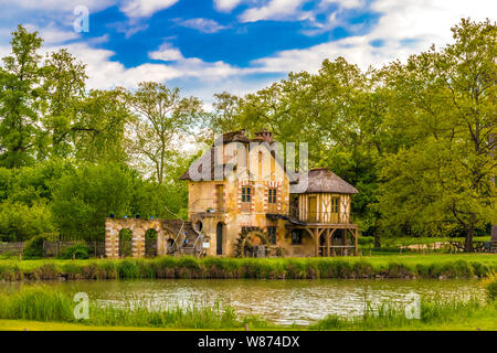 Picturesque view of the Mill, a rustic building in the Queen's Hamlet, surrounded by trees under a blue sky in front of a lake in the park of the... Stock Photo
