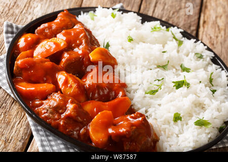 Serve braised veal with apples in tomato sauce with rice garnish close up on a plate on the table. horizontal Stock Photo