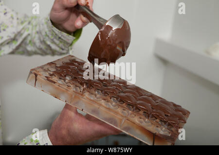 pouring molten chocolate into a mould to make chocolates. Stock Photo