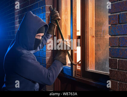 Burglar breaking into a home through the window with a crowbar Stock Photo