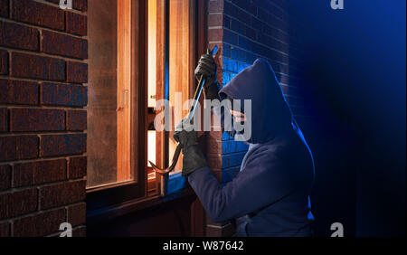 Burglar breaking into a home through the window with a crowbar Stock Photo