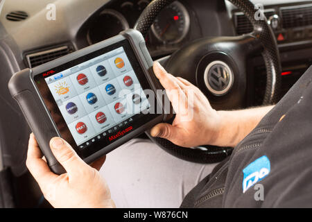 Garage: car mechanics. Worker using the touchscreen tablet of a car diagnostic tool in the front seat of a Volkswagen car, to detect any potential eng Stock Photo