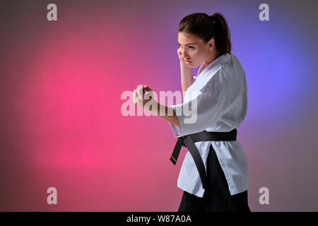 Athletic woman in traditional kimono is practicing karate in studio.